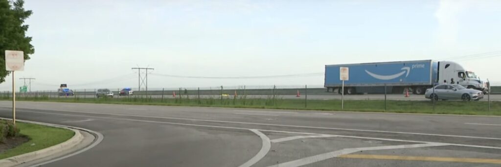 Image of an Amazon semi-truck involved in a crash on I-75 in Weston, with police cars and traffic cones near the scene.